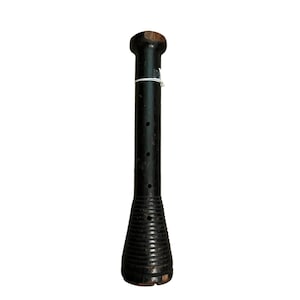 Op de afbeelding: Een zwarte houten spoel met een afgeronde bovenkant en een uitlopende, geribbelde basis. De spoel heeft een reeks kleine gaatjes langs de cilindrische behuizing en is vastgebonden met een wit touwtje. Het hout heeft een verweerde uitstraling.