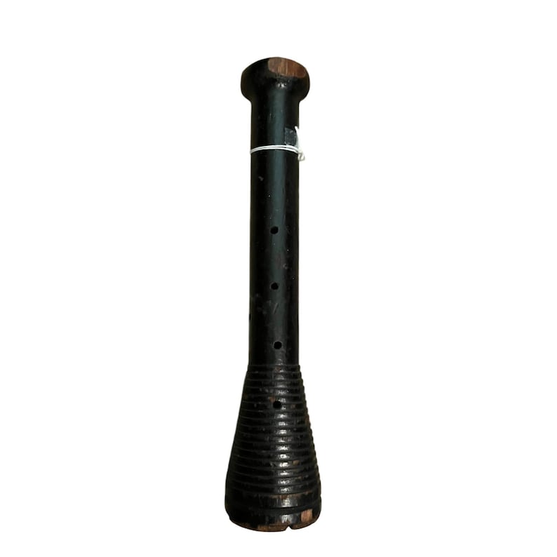 Op de afbeelding: Een zwarte houten spoel met een afgeronde bovenkant en een uitlopende, geribbelde basis. De spoel heeft een reeks kleine gaatjes langs de cilindrische behuizing en is vastgebonden met een wit touwtje. Het hout heeft een verweerde uitstraling.
