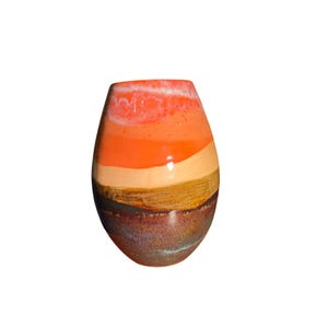 May include: A colorful, handcrafted ceramic vase with a unique, layered design. The vase features horizontal bands of orange, peach, and brown hues, creating a striking visual effect. The vase is approximately 8 inches tall, with a wide base and a narrower opening.