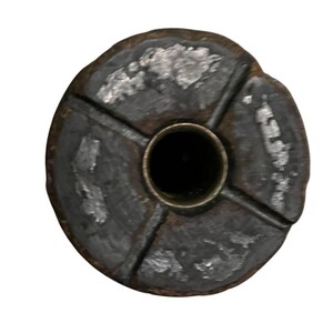 Op de afbeelding: Een donker, cirkelvormig object met een centraal gat, gezien van bovenaf. Het object is verdeeld in vier secties door kruisende lijnen. Het oppervlak heeft een ruwe, getextureerde uitstraling met lichtere vlekken.