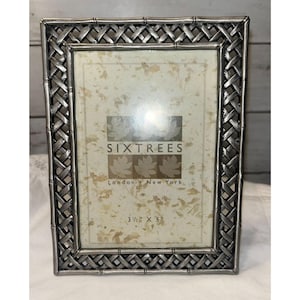 May include: A rectangular picture frame with a metallic silver finish and a woven lattice border design. The insert displays the text SIXTREES London New York and the dimensions 3 1/2 inches by 5 inches on a cream-colored background with leaf motifs.