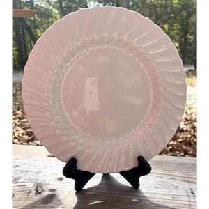May include: A white, round dinner plate with a spiral design around the rim. The plate is displayed on a black stand, showcasing its elegant form. The plate's surface reflects light, highlighting its smooth texture.
