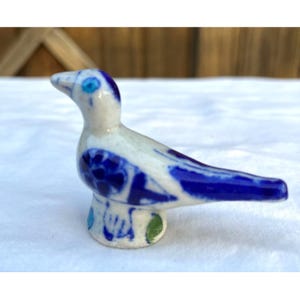 May include: A ceramic bird figurine in white and blue. The bird has a blue beak, eye, and wing details. The base features blue and green accents. The figurine is a decorative item.