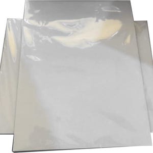 May include: A stack of white canvas panels, wrapped in clear plastic, are displayed. The panels are rectangular and appear unused, ready for artistic projects. The plastic wrap gives a glossy appearance. The panels are likely for painting or mixed media.
