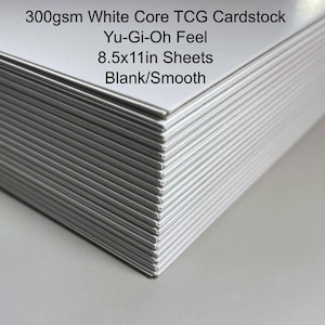 May include: A stack of white cardstock sheets. The text on the image reads: 300gsm White Core TCG Cardstock, Yu-Gi-Oh Feel, 8.5x11in Sheets, Blank/Smooth. The sheets are blank and smooth.