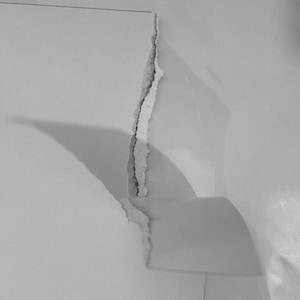 May include: A close-up of torn white paper, showing a rough, irregular edge. The paper is creased, with shadows creating a sense of depth. The image is in monochrome, with varying shades of grey.