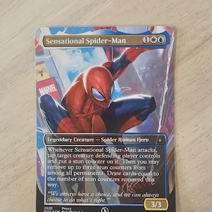 May include: A Sensational Spider-Man trading card featuring the superhero in a dynamic pose. The card has a blue and red color scheme, with the Marvel logo visible. Text includes "Legendary Creature - Spider Human Hero" and card details.