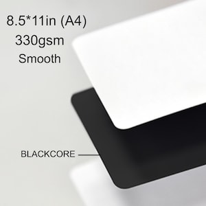May include: A stack of smooth, white paper sheets with a black core, labeled as 21.6 x 27.9 cm (A4) and 330gsm. The text "BLACKCORE" is visible. The paper appears to be high-quality and suitable for various uses.