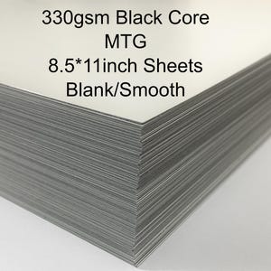 May include: A stack of blank white 8.5 x 11 inch sheets with a black core. The text on the top sheet reads "330gsm Black Core MTG 8.5*11inch Sheets Blank/Smooth."