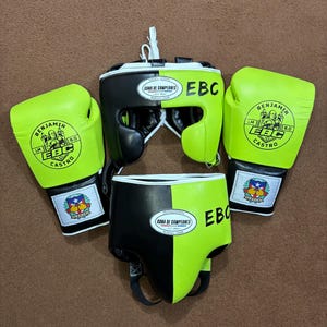 Könnte beinhalten: Ein Box-Set mit einem schwarzen und neongrünen Kopfschutz, Boxhandschuhen und Shorts. Die Handschuhe und Shorts tragen den Text "BENJAMIN EBC CASTRO" und "CONA DE CAMPEONES". Das Set ist für Boxtraining und Wettkämpfe konzipiert.