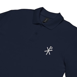 Könnte beinhalten: Marineblaues Poloshirt mit einem weißen, gestickten Symbol auf der linken Brust. Das Shirt hat einen klassischen Kragen und eine Knopfleiste mit drei Knöpfen. Das Gildan-Markenschild ist sichtbar.