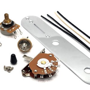 May include: A collection of guitar parts, including potentiometers, a switch, a capacitor, a jack, screws, a chrome control plate, and wires. The components are arranged on a white surface.