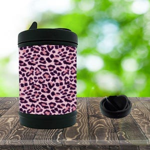 May include: A cylindrical insulated food container featuring a pink and dark purple leopard print pattern. The container has a solid black lid with a small handle tab and a separate matching black circular lid component placed to the right side.