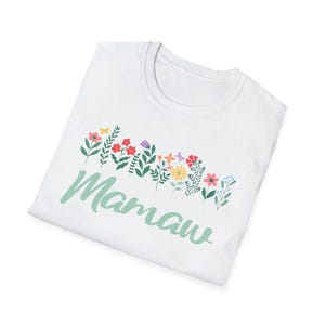 May include: White t-shirt with the word "Mamaw" in a light green script font. Above the word is a colorful floral design with red, pink, yellow, and purple flowers and green leaves. The shirt is folded.
