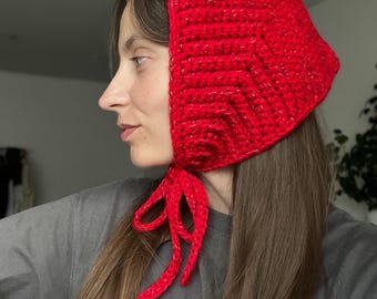 Peut inclure: Un bonnet au crochet rouge vif avec un motif de point texturé. Le bonnet est doté d'une fermeture à nouer et est fabriqué avec un fil à la brillance métallique subtile. Cet accessoire est élégant.