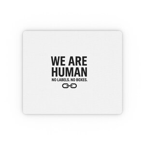 Peut inclure: Un tapis de souris rectangulaire blanc avec le texte "WE ARE HUMAN" en lettres noires grasses. En dessous, le texte indique "NO LABELS. NO BOXES." Un symbole de maillon de chaîne noir est en bas. Le tapis de souris a une surface lisse.