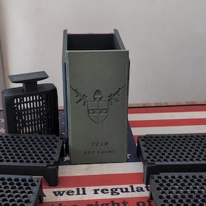 May include: An assortment of black accessories, including a rectangular container with text and a shield design, and several trays with a grid pattern. The items are on a surface with a red, white, and blue pattern.