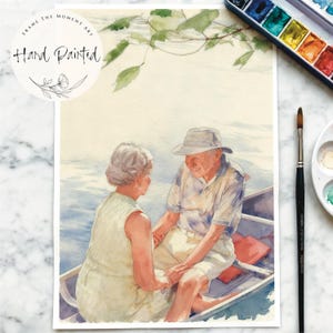 Pode incluir: Impress&atilde;o de arte em aquarela pintada &agrave; m&atilde;o retratando um casal de idosos em um barco em um lago. A obra de arte apresenta cores suaves, uma atmosfera serena e o texto "Frame the Moment Art" e "Hand Painted". Uma paleta de aquarela e um pincel s&atilde;o vis&iacute;veis.