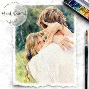 Könnte beinhalten: Aquarellmalerei eines sich umarmenden Paares, wobei die Frau den Betrachter ansieht. Das Kunstwerk ist handgemalt, mit den Worten "Frame the Moment Art" und "Hand Painted" sichtbar. Das Gemälde hat eine weiche, romantische Ausstrahlung, mit einer Palette aus Grün-, Weiß- und Hauttönen.