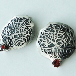 May include: A pair of silver earrings with a delicate, intricate design and a red gemstone accent.