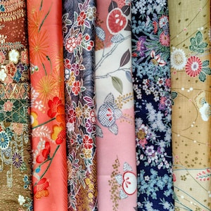 May include: A collection of rolled fabric with floral patterns in various colors. The fabrics include designs with red, orange, pink, and blue flowers, as well as geometric and striped patterns. The overall aesthetic is inspired by Japanese textiles.