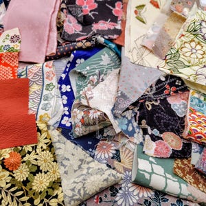 Könnte beinhalten: Eine Sammlung bunter Stoffreste mit floralen und geometrischen Mustern. Die Stoffe weisen eine Vielzahl von Farben auf, darunter Rot, Schwarz, Blau und Creme, mit detaillierten Designs. Ideal für Quilt- oder Bastelprojekte.