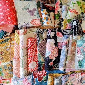 Pode incluir: Uma coleção de amostras de tecido dobradas com diversos padrões, incluindo motivos florais, formas geométricas e designs abstratos em cores vibrantes como vermelho, azul, verde, amarelo, rosa e preto com superfícies texturizadas.
