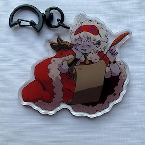 May include: A clear acrylic keychain featuring a cartoon character in a red robe with white fur trim, holding a quill and scroll. The keychain has a black clasp for attaching to bags or keys.