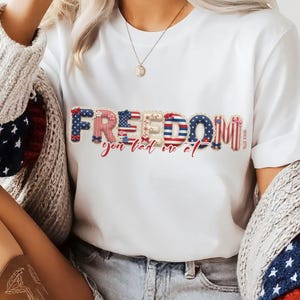 May include: A white t-shirt featuring the word FREEDOM in a patriotic red, white, and blue patterned font, with the text you had me at written in red cursive below it and the small text SINCE 1776 printed vertically on the right side of the graphic.