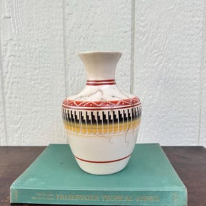 May include: A cream-colored ceramic vase with a narrow neck and a wide body. The vase features a decorative band with red, black, and yellow geometric patterns, including stepped designs and thin horizontal lines, accented by fine dark crackle lines.