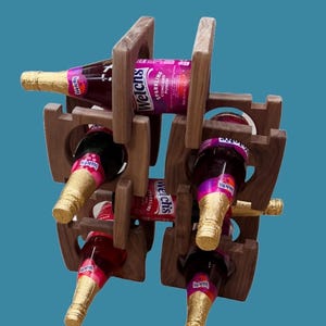 May include: A wooden wine rack holding six bottles of Welch's Sparkling Concord Punch. The bottles have gold foil around the necks and are arranged in a vertical, geometric pattern. The rack is made of dark wood.