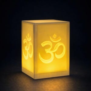 Puede incluir: Una caja cuadrada iluminada con el símbolo Om en cada lado. La caja emite una luz amarilla cálida, creando un brillo suave. El símbolo Om es un icono espiritual en el hinduismo, el budismo y el jainismo.