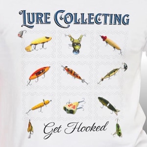 May include: White t-shirt featuring a collection of colorful fishing lures. The shirt has the text "Lure Collecting" above the lures and "Get Hooked" below. The lures are in various shapes and colors, including yellow, red, and green.