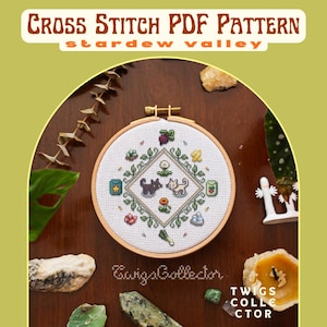 May include: A cross-stitch PDF pattern for "Stardew Valley" featuring a circular embroidery hoop with a stitched design of two cats, flowers, and leaves. The text "Cross Stitch PDF Pattern" and "Stardew Valley" are at the top.