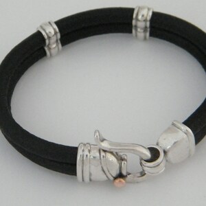 K&ouml;nnte beinhalten: Ein schwarzes Lederarmband mit silbernen Akzenten und einem silbernen Verschluss. Das Armband hat ein schlichtes Design und ist ein klassisches Schmuckst&uuml;ck.