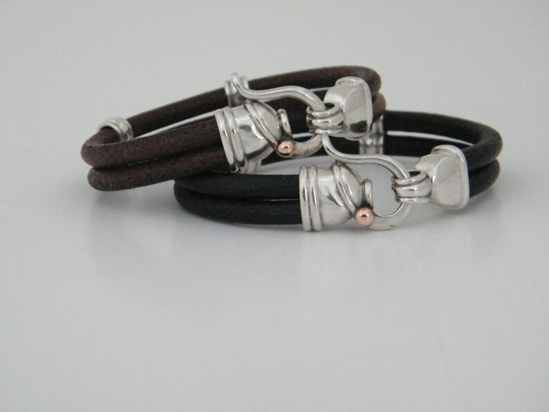 K&ouml;nnte beinhalten: Zwei Lederarmb&auml;nder mit silbernen und goldenen Verschl&uuml;ssen. Die Armb&auml;nder sind braun und schwarz.