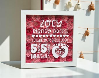 May include: A white framed shadow box filled with pink paper roses. The box displays the name "Zoey Ribeiro Breese", birthdate, weight of 5 pounds 5 ounces, and length of 18 inches. A heart with footprints and the time 6:54 PM is also included.