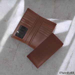 Peut inclure: Un portefeuille en cuir marron, ouvert pour montrer plusieurs fentes pour cartes et une fenêtre d'identification transparente. Le portefeuille est posé sur une surface de couleur claire, avec le portefeuille fermé à côté. La marque "ChanifalD" est visible en bas à droite.