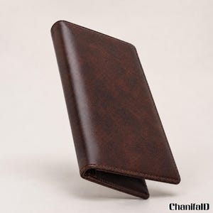 May include: A dark brown, rectangular, bi-fold wallet with a smooth, matte finish and visible stitching along the edges. The wallet is positioned at an angle, showing its folded structure. The text ChanifalD is printed in black in the bottom corner.