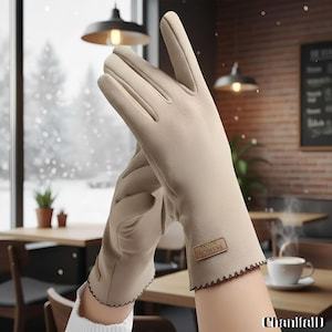 Może przedstawiać: Beżowe rękawiczki z falistym brzegiem i małą etykietą "FASHION GLOVES". Rękawiczki są prezentowane w otoczeniu kawiarni z widokiem na zaśnieżone otoczenie. Rękawiczki wydają się być wykonane z miękkiego, ciepłego materiału.