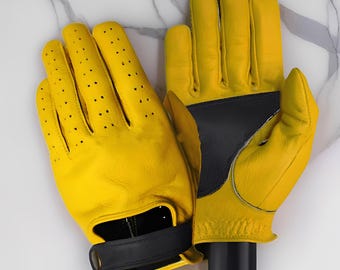 May include: A pair of bright yellow leather gloves with black accents. The gloves have small perforations on the fingers and a black strap closure. The gloves are designed for sports or driving.