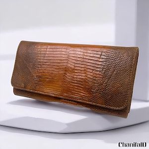May include: A brown leather wallet with a reptile skin texture. The wallet has a rectangular shape with a fold-over flap. The color is a mix of light and dark brown tones.