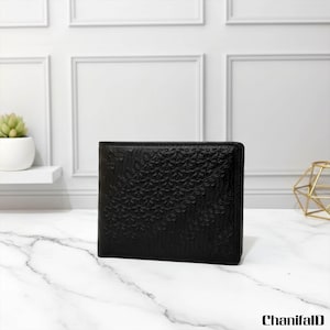 May include: A black leather wallet with a textured floral design. The bi-fold wallet is rectangular. The background features a white wall with decorative moulding and a marble surface.
