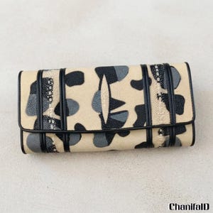 May include: A beige wallet with a black and grey abstract pattern. The wallet has a rectangular shape with a flap closure and black trim. The design includes various shapes and textures.
