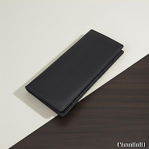 Peut inclure: Un portefeuille en cuir noir de forme rectangulaire. Le portefeuille est fermé et présente une surface lisse. Le fond est blanc et marron foncé.