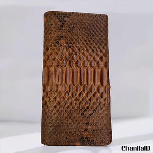 May include: A rectangular, brown wallet with a snakeskin pattern. The wallet has a textured surface and a natural color palette, with darker brown accents. The design is reminiscent of reptile skin, with a scale-like appearance.