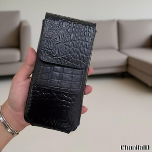May include: Black leather phone case with a crocodile skin texture. The case has a flap closure and a rectangular shape. The case is held in a hand. The brand name "ChanifalD" is in the bottom right corner.