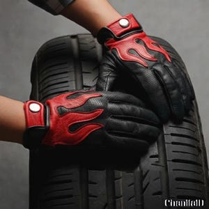 Peut inclure: Gants en cuir noir avec des flammes rouges. Les gants ont un design perforé et une fermeture à bouton-pression au poignet. Les gants sont présentés sur un pneu noir.