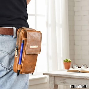 Könnte beinhalten: Eine braune Gürteltasche aus Leder mit einem Reißverschluss-Hauptfach und einer Frontklappe. Ein blauer Stift befindet sich in einer Seitentasche. Die Tasche ist an einem braunen Gürtel befestigt. Der Text "PADRA & GASIK" ist auf der Frontklappe.