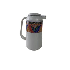 Puede incluir: Una jarra térmica blanca con cuerpo cilíndrico y asa lateral. La sección superior está decorada con una banda horizontal que muestra un colorido patrón de mosaico con formas geométricas y motivos florales en rojo, azul, verde y dorado.